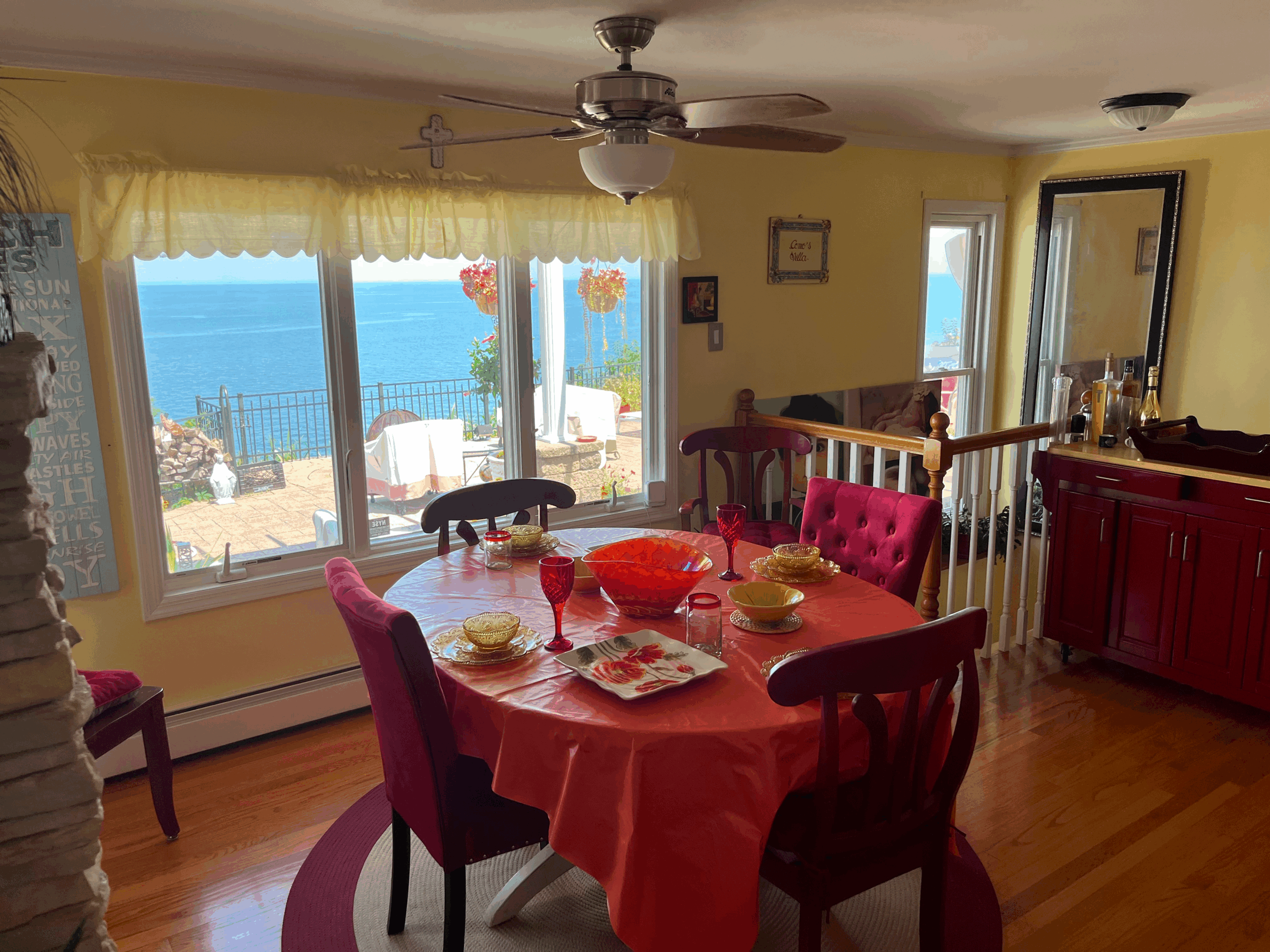 Dining area with a red tablecloth and ocean view through large windows.
