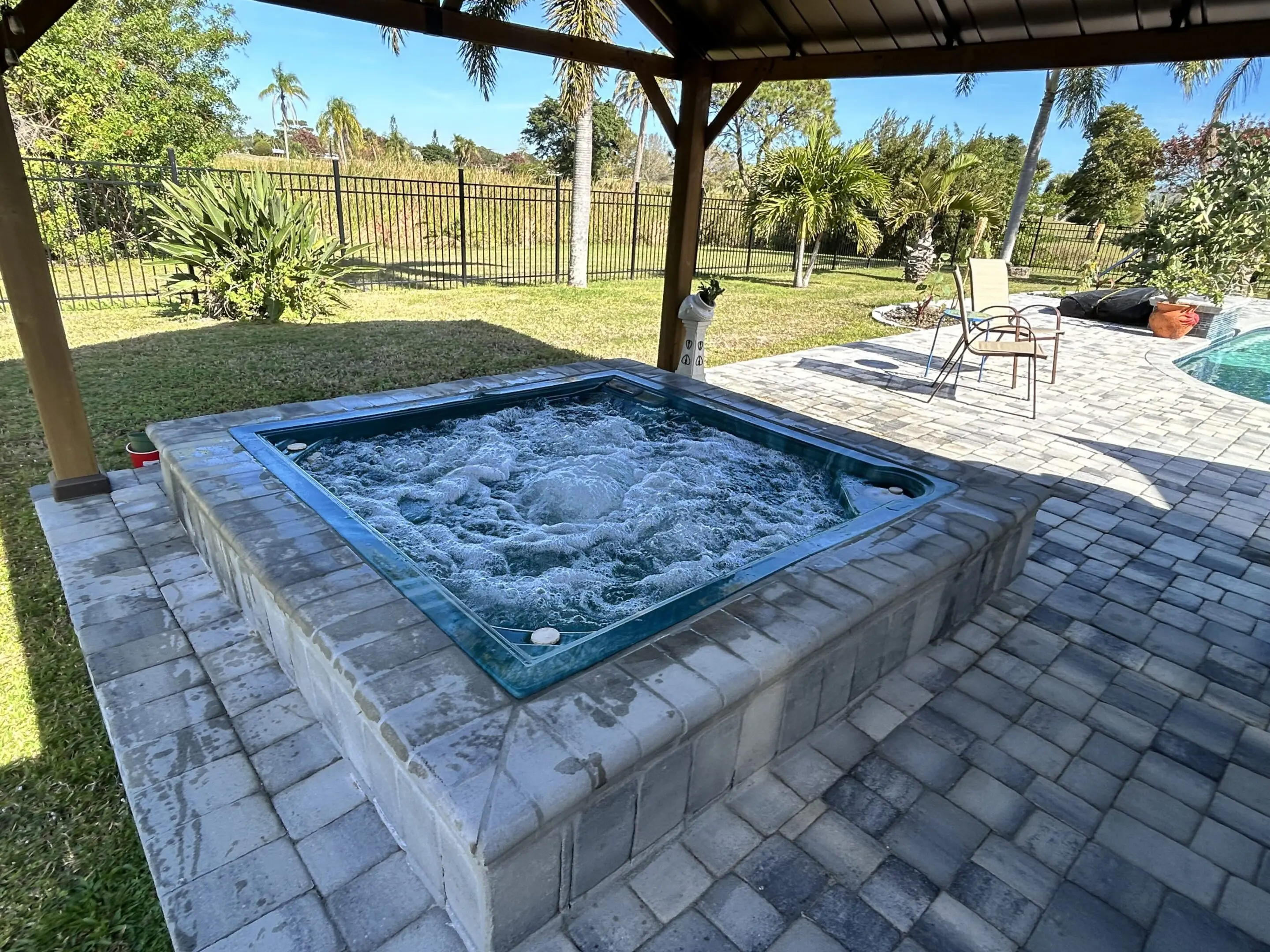 Outdoor hot tub bubbling under a shaded patio with a garden view.