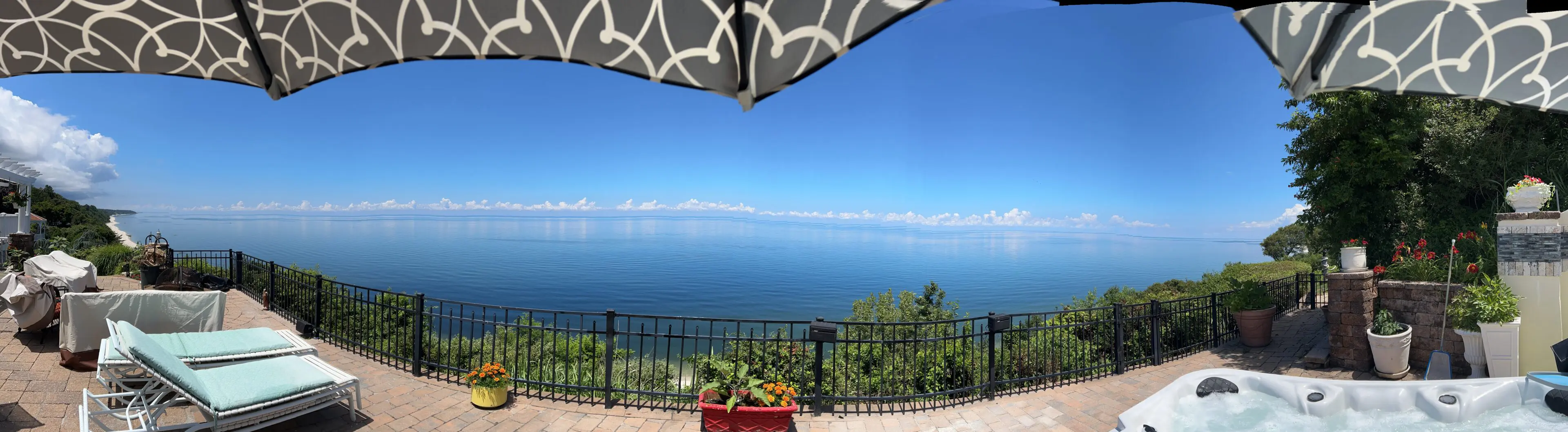 Clear blue sky over a calm sea with a patio umbrella and railing in view.